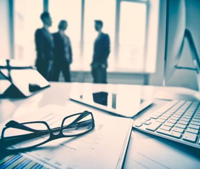 Modern devices, documents, eyeglasses on the foreground, unrecognized businessmen on the background